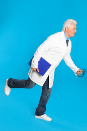 Senior doctor with clipboard and stethoscope running on light blue background