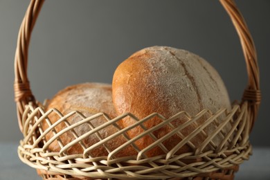 Photo of Wicker basket with fresh bread on grey table, closeup