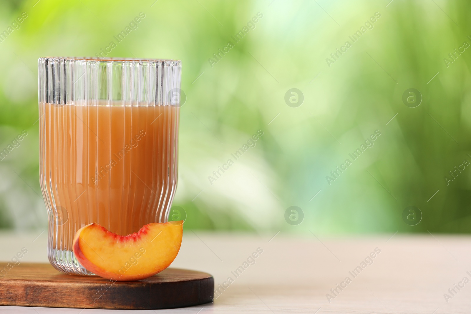Photo of Glass of tasty peach juice and fresh fruit on white table outdoors, closeup. Space for text