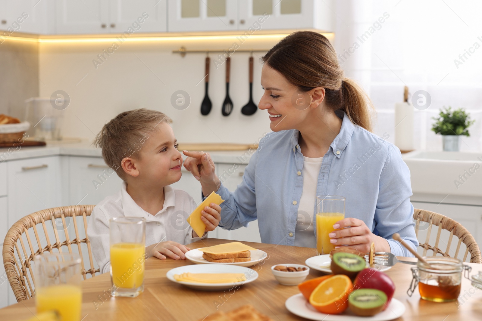 Photo of Mother and her cute little son having breakfast at table in kitchen