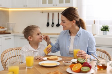 Photo of Mother and her cute little son having breakfast at table in kitchen