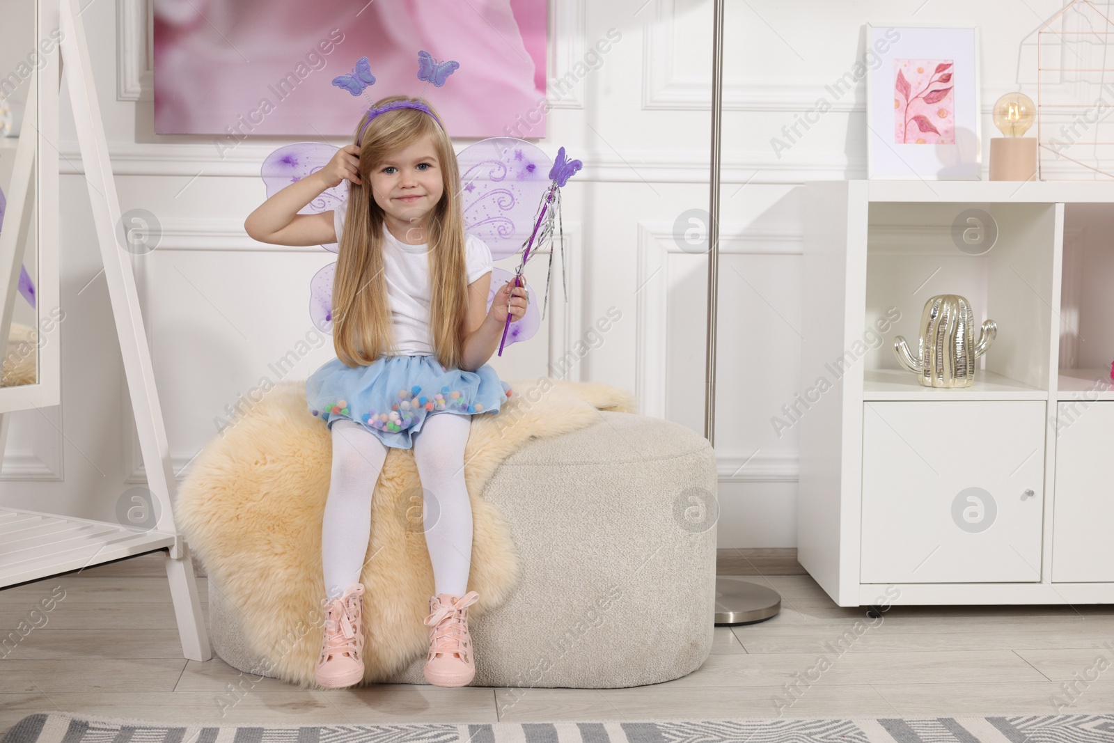 Photo of Cute little girl in fairy costume with violet wings and magic wand at home, space for text