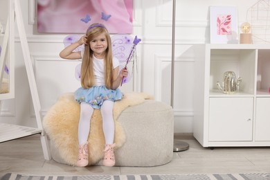 Cute little girl in fairy costume with violet wings and magic wand at home, space for text