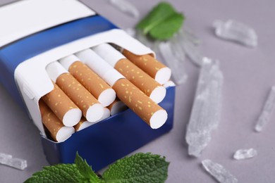 Photo of Pack of cigarettes, menthol crystals and mint leaves on grey background, closeup