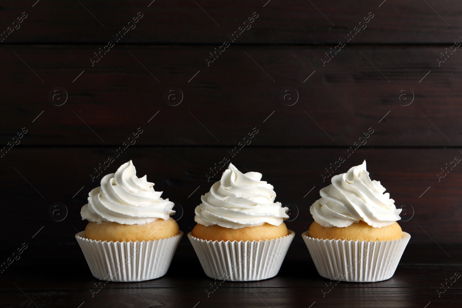 Photo of Delicious cupcakes with white cream on wooden table. Space for text