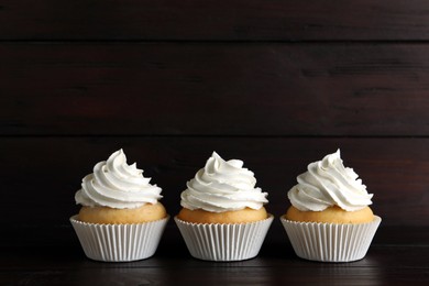 Photo of Delicious cupcakes with white cream on wooden table. Space for text