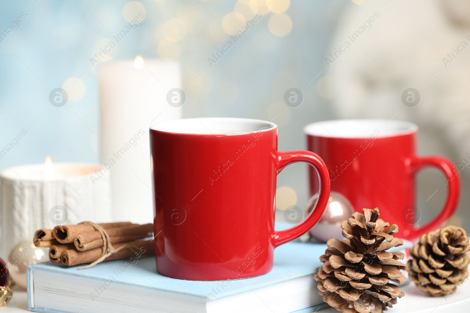 Photo of Cups of hot winter drink and Christmas decoration on table against blurred lights