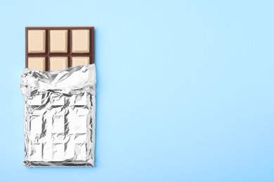 Photo of Tasty chocolate bar on light blue background, top view. Space for text