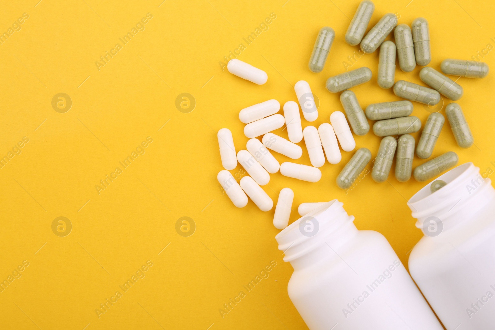 Photo of Jars with different vitamin capsules on yellow background, flat lay. Space for text