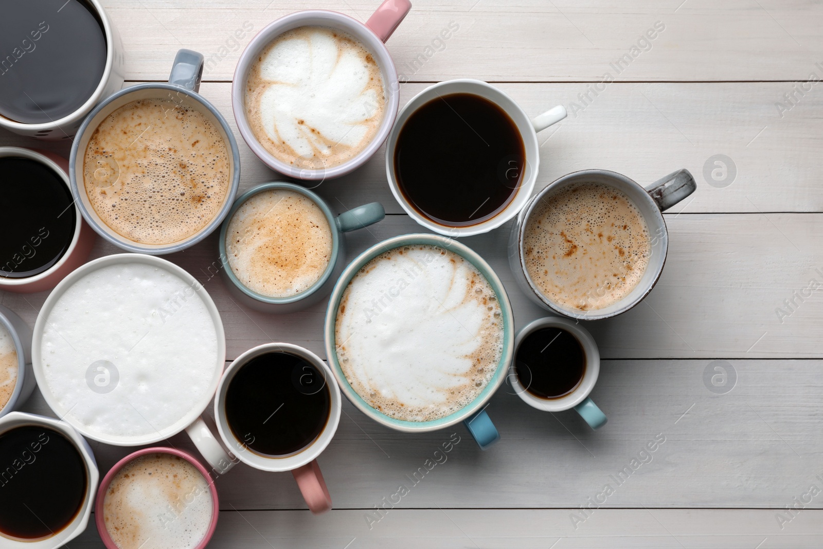 Photo of Many different cups with aromatic hot coffee on white wooden table, flat lay