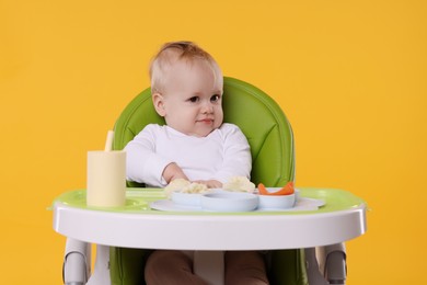 Photo of Cute little baby with healthy food in high chair on orange background