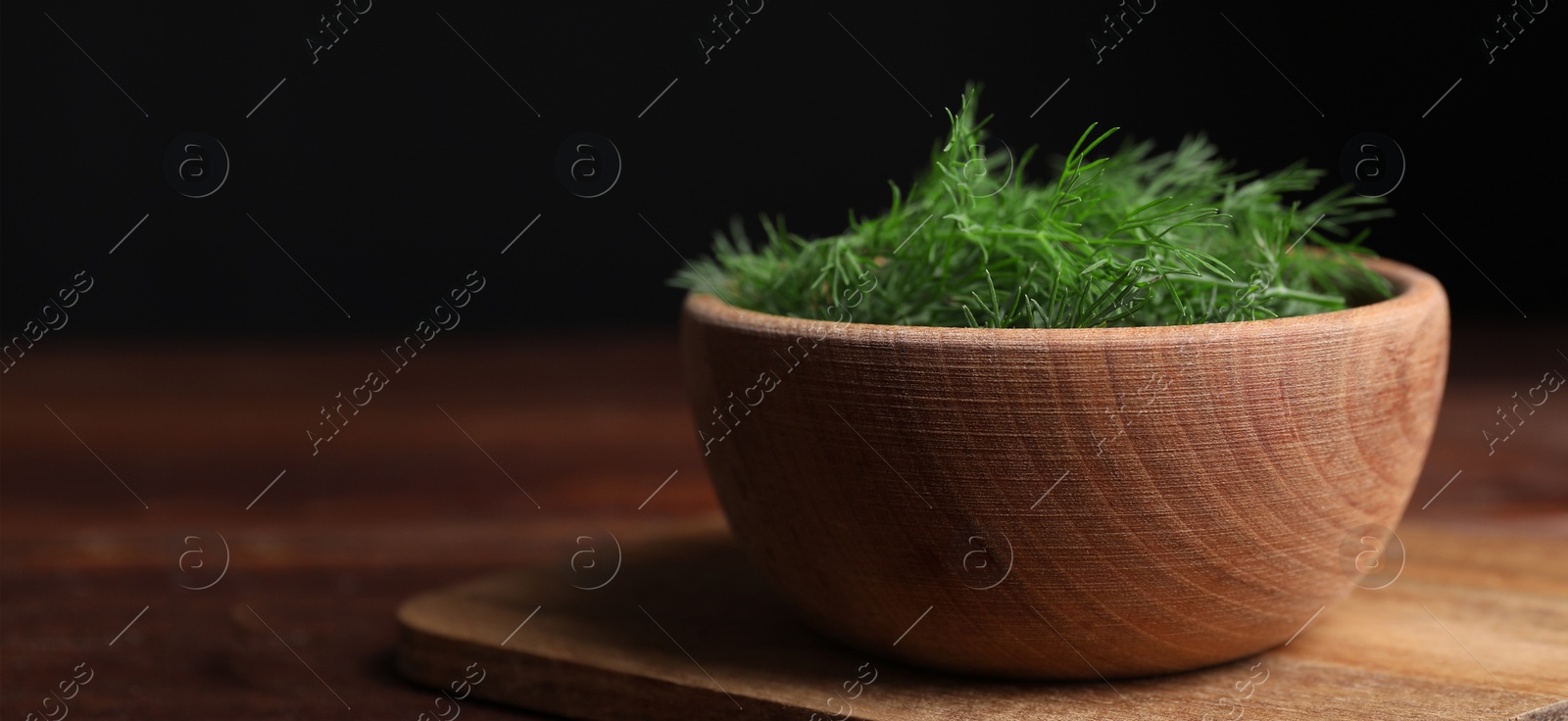 Image of Fresh dill in bowl on wooden table against black background. Banner design with space for text