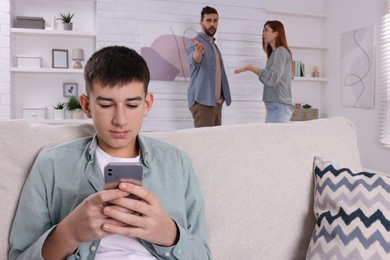 Photo of Unhappy teenage boy scrolling through phone while his parents arguing on background. Problems at home