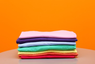 Photo of Stack of rainbow clothes on table against color background