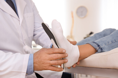 Male orthopedist fitting insole on patient's foot in clinic, closeup