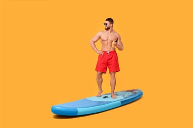 Man with refreshing drink posing on SUP board against orange background