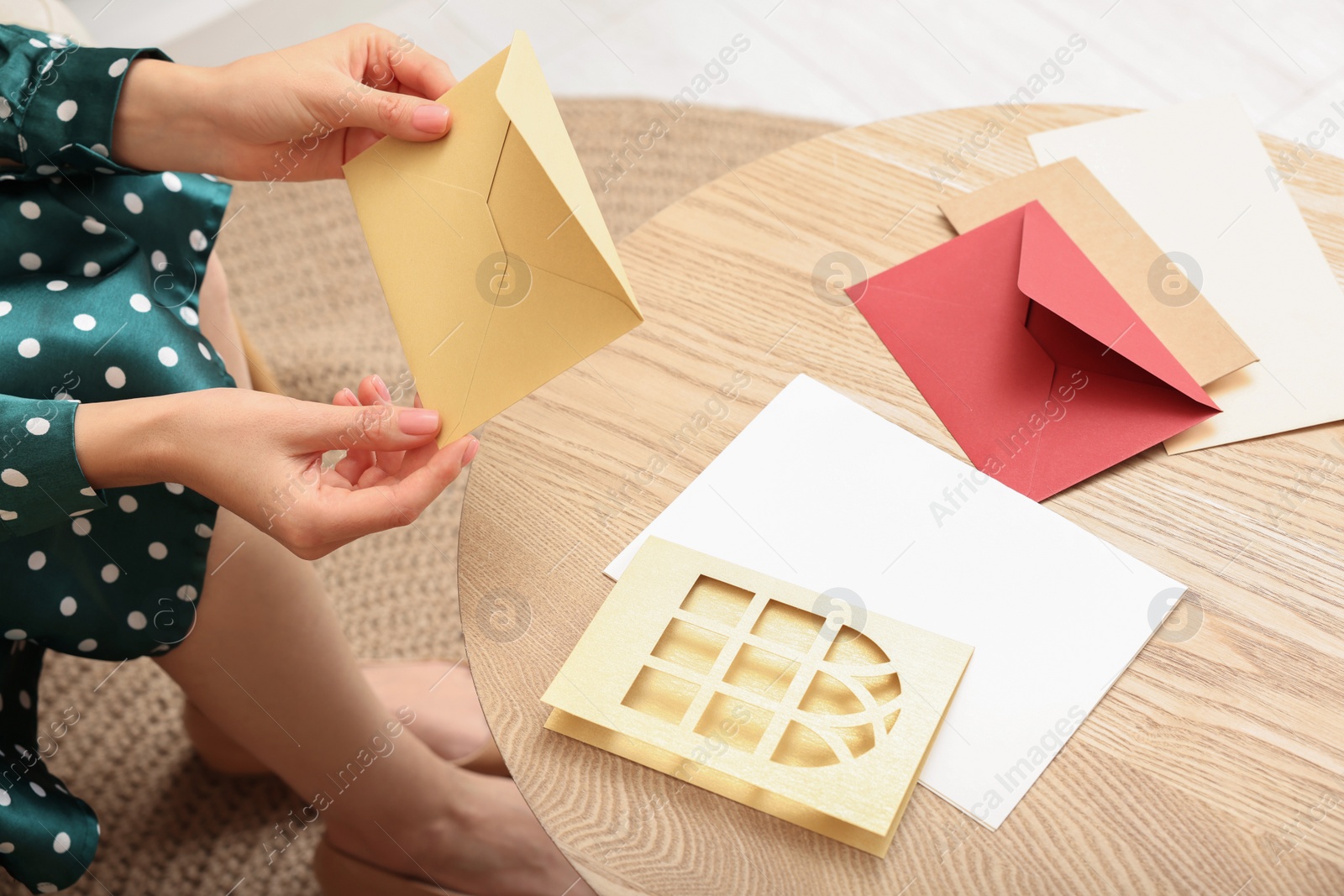 Photo of Woman holding greeting card at wooden table in living room, closeup