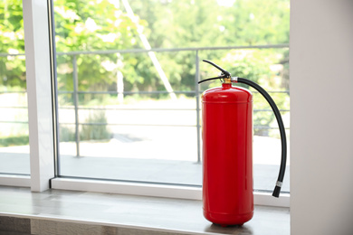 Photo of Fire extinguisher near window indoors. Space for text