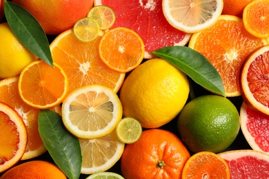 Photo of Sliced and whole citrus fruits with leaves as background, top view