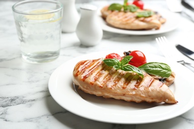 Photo of Tasty grilled chicken fillet with green basil and tomatoes on white marble table, closeup
