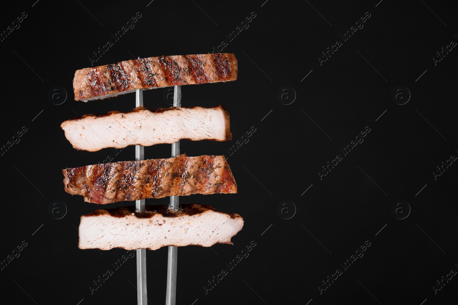 Photo of Carving fork with cut grilled pork steak pieces against black background. Space for text