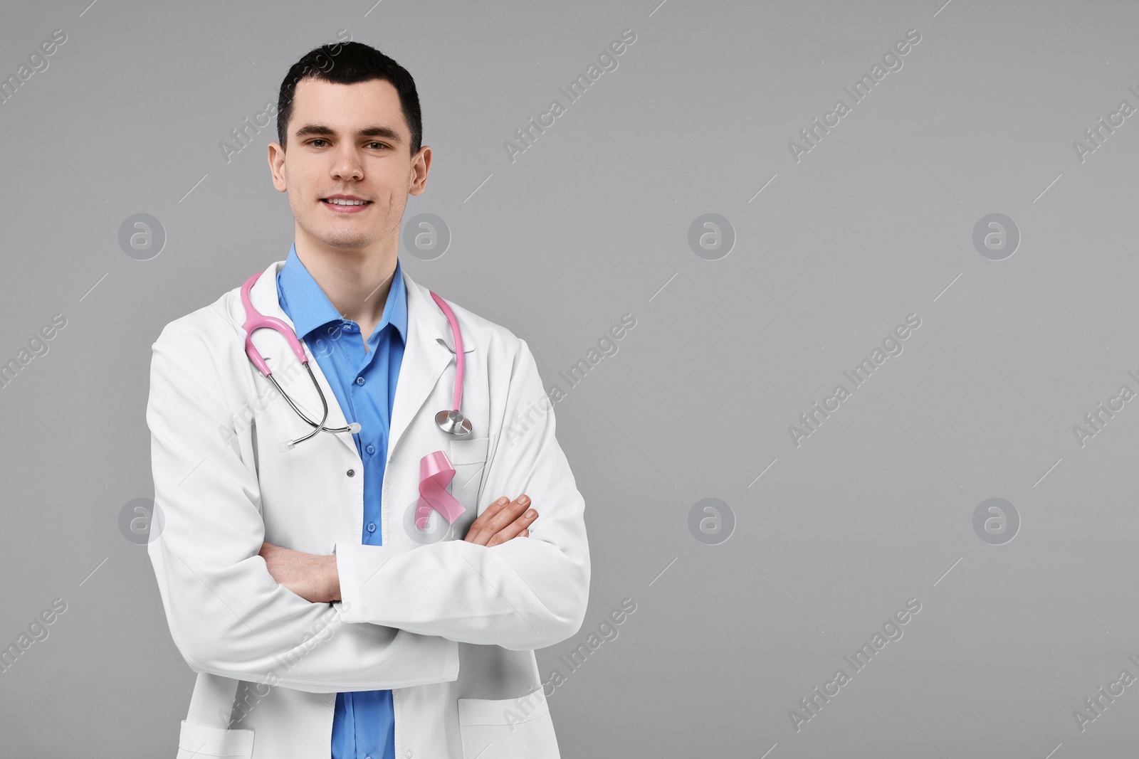 Photo of Portrait of smiling mammologist with pink ribbon and stethoscope on grey background. Space for text