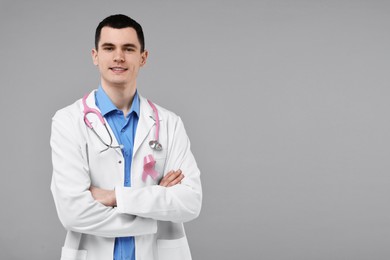 Photo of Portrait of smiling mammologist with pink ribbon and stethoscope on grey background. Space for text