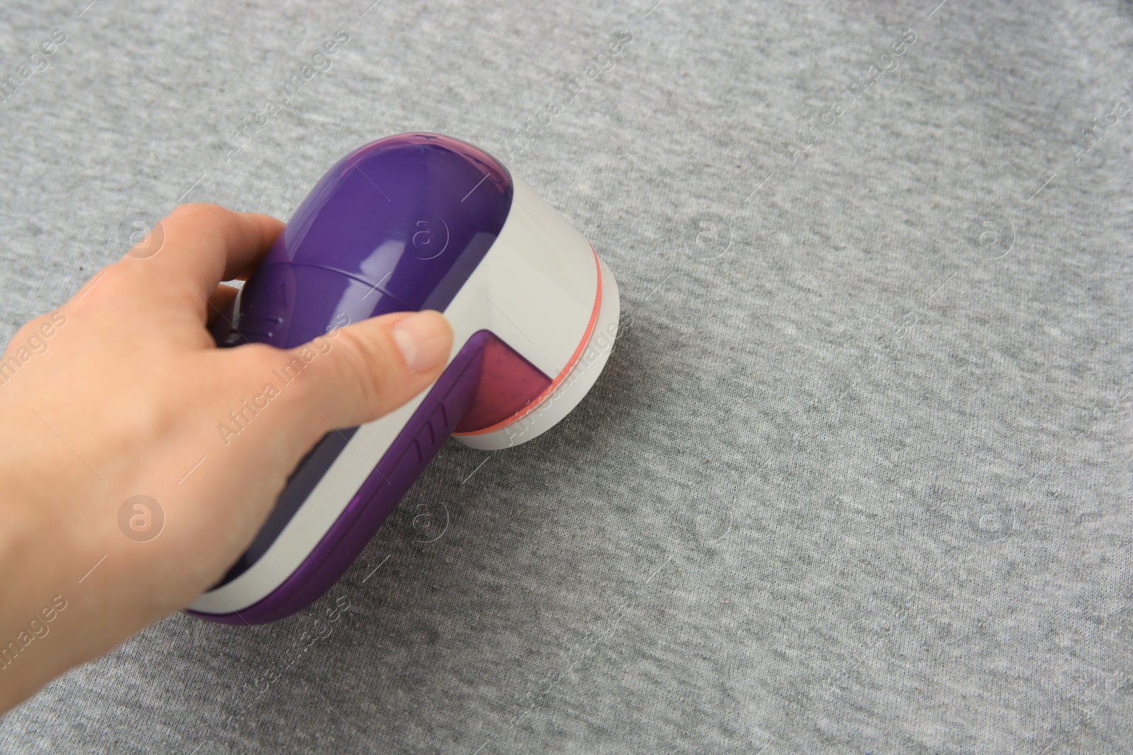 Photo of Woman using fabric shaver on light grey cloth with lint, closeup. Space for text