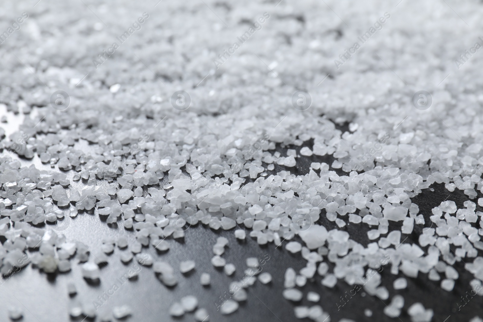 Photo of Scattered natural salt on black table, closeup