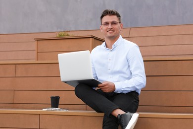 Handsome man using laptop on bench outdoors