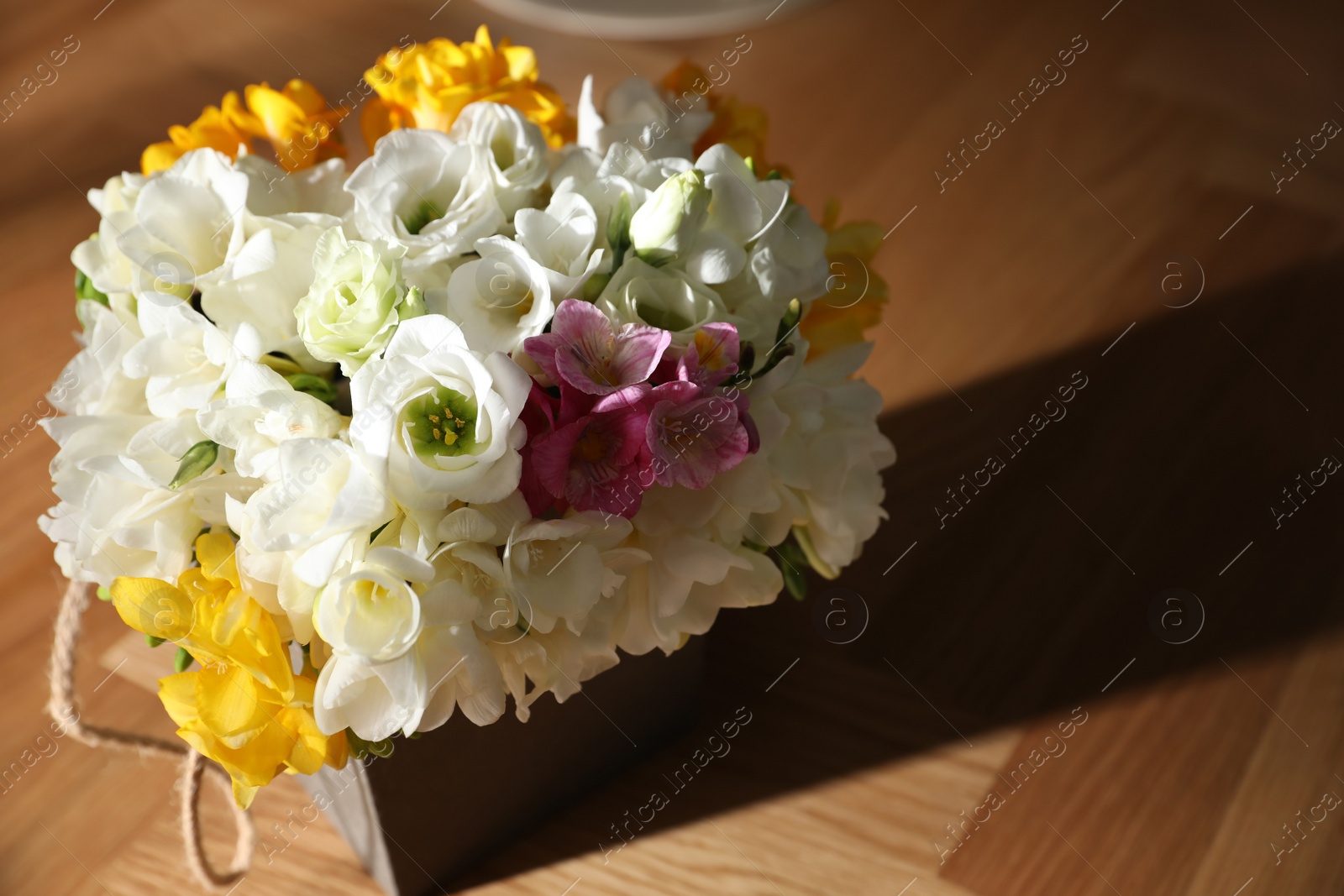 Photo of Beautiful bouquet with spring freesia flowers on sunlit wooden table