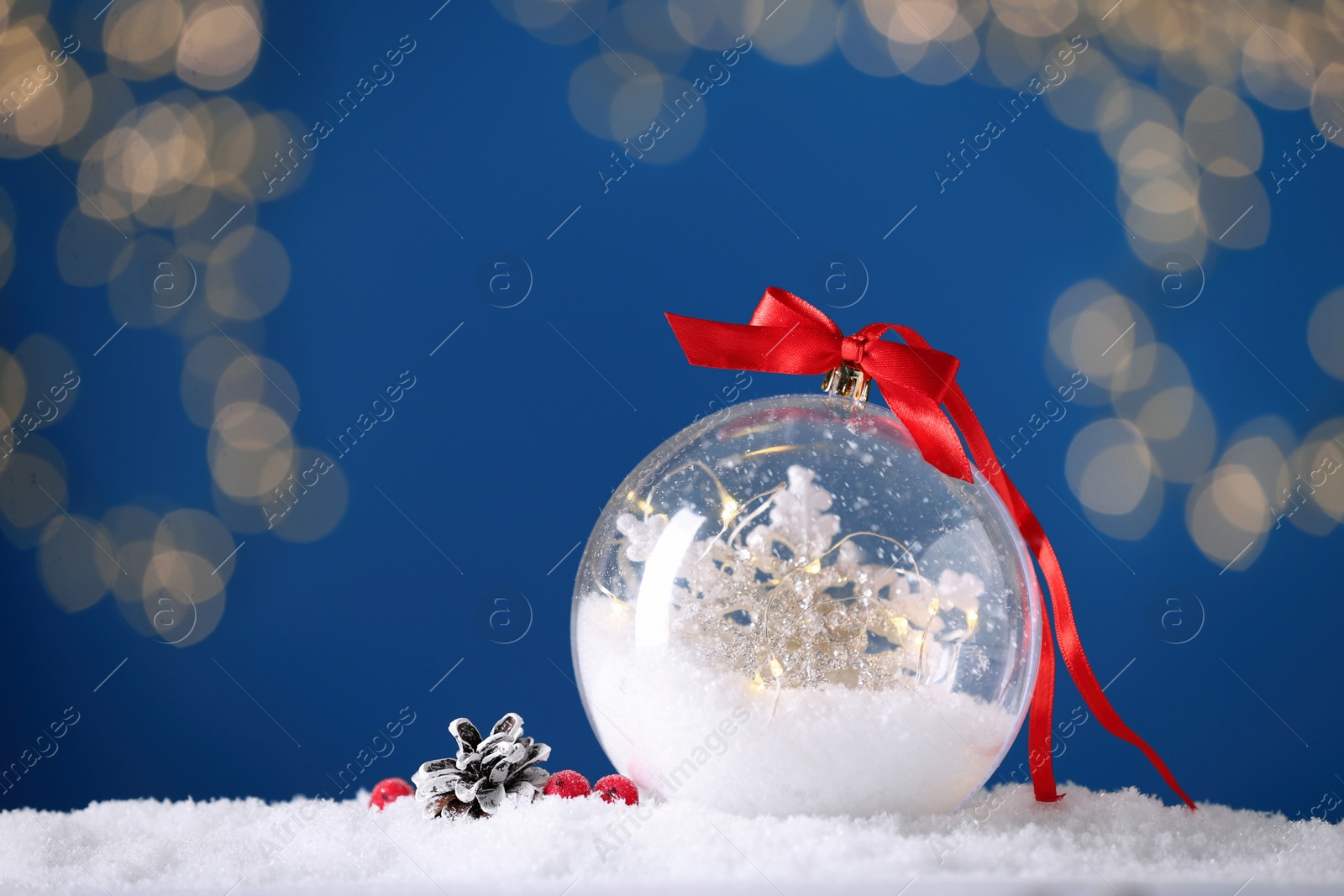 Photo of Decorative snow globe with red ribbon against blurred festive lights, closeup