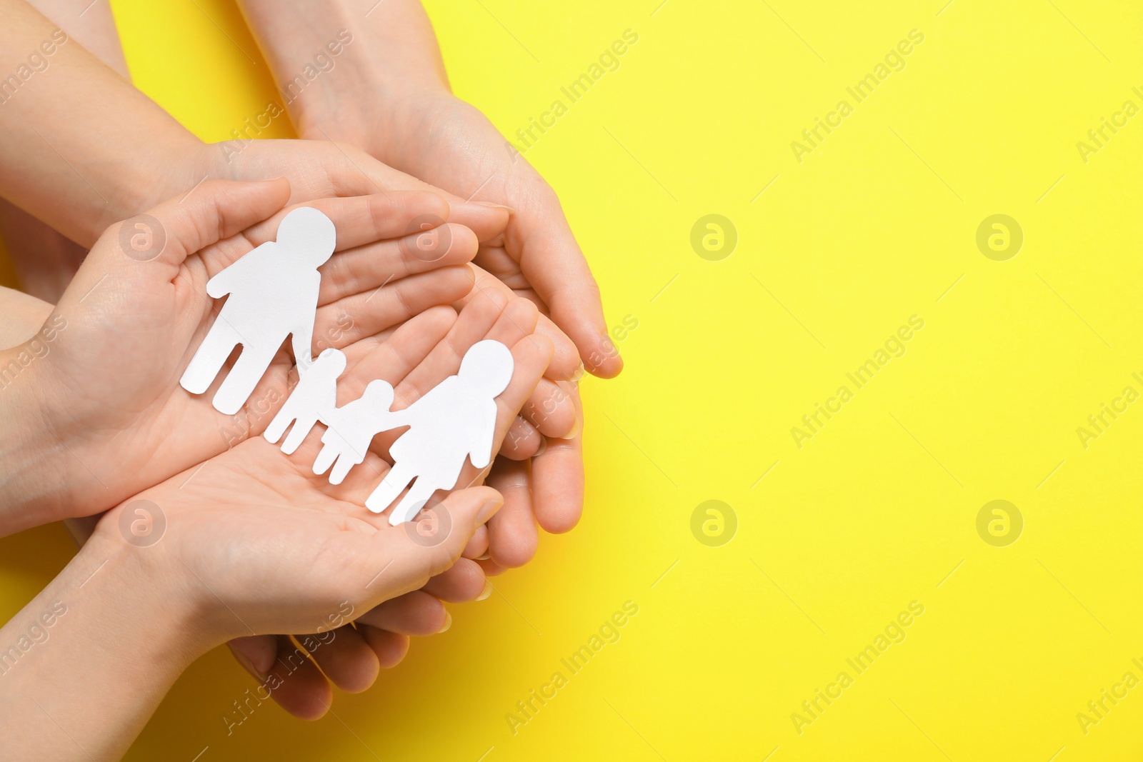 Photo of People holding paper family cutout on yellow background, top view. Space for text
