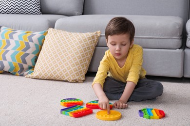 Photo of Little boy playing with pop it fidget toys on floor at home