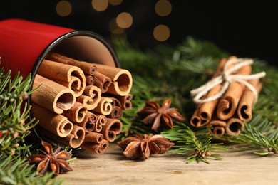 Many cinnamon sticks, anise stars and fir branches on wooden table, closeup