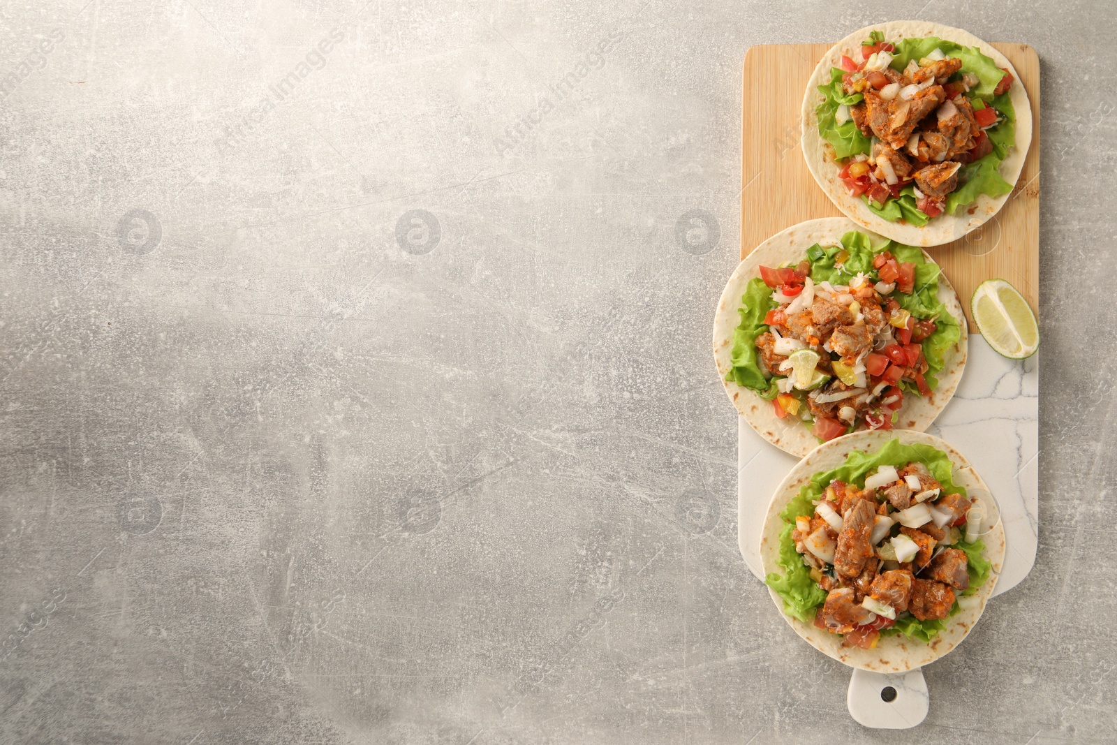 Photo of Delicious tacos with vegetables, meat and lime on grey textured table, top view. Space for text