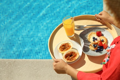Young woman with delicious breakfast on tray near swimming pool, closeup. Space for text