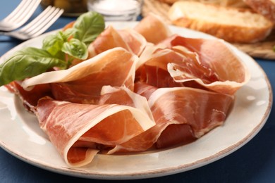 Slices of tasty cured ham and basil on plate, closeup
