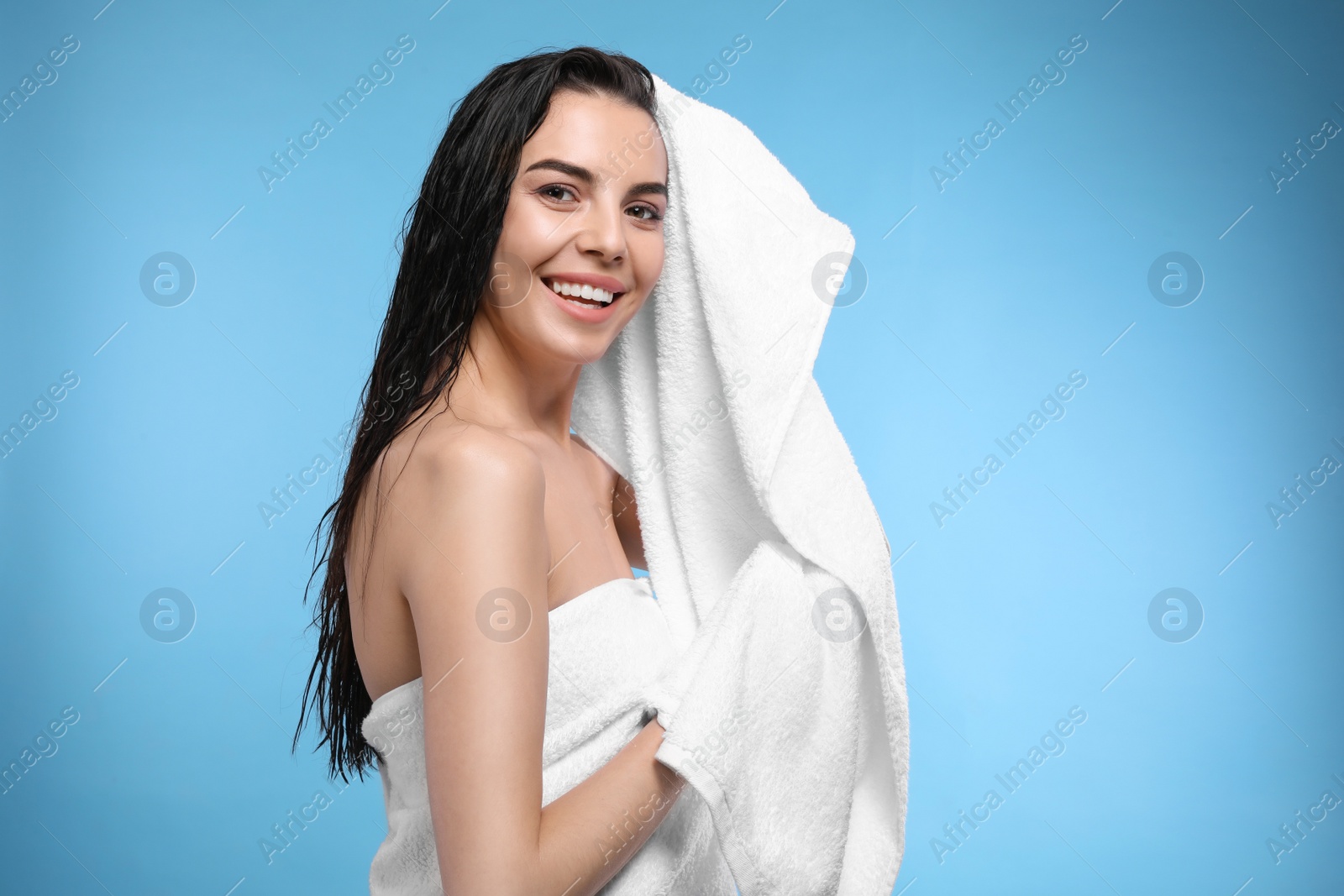 Photo of Happy young woman drying hair with towel after washing on light blue background