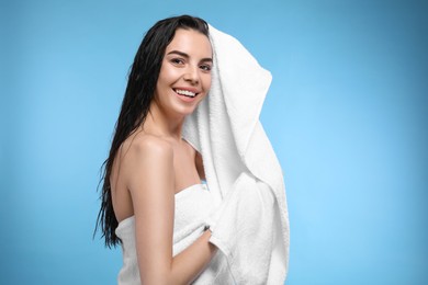 Happy young woman drying hair with towel after washing on light blue background