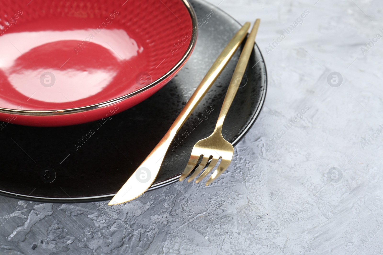 Photo of Clean plates, bowl and cutlery on gray textured table, closeup. Space for text