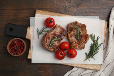 Delicious fried meat with rosemary, tomatoes and spices on wooden table, flat lay