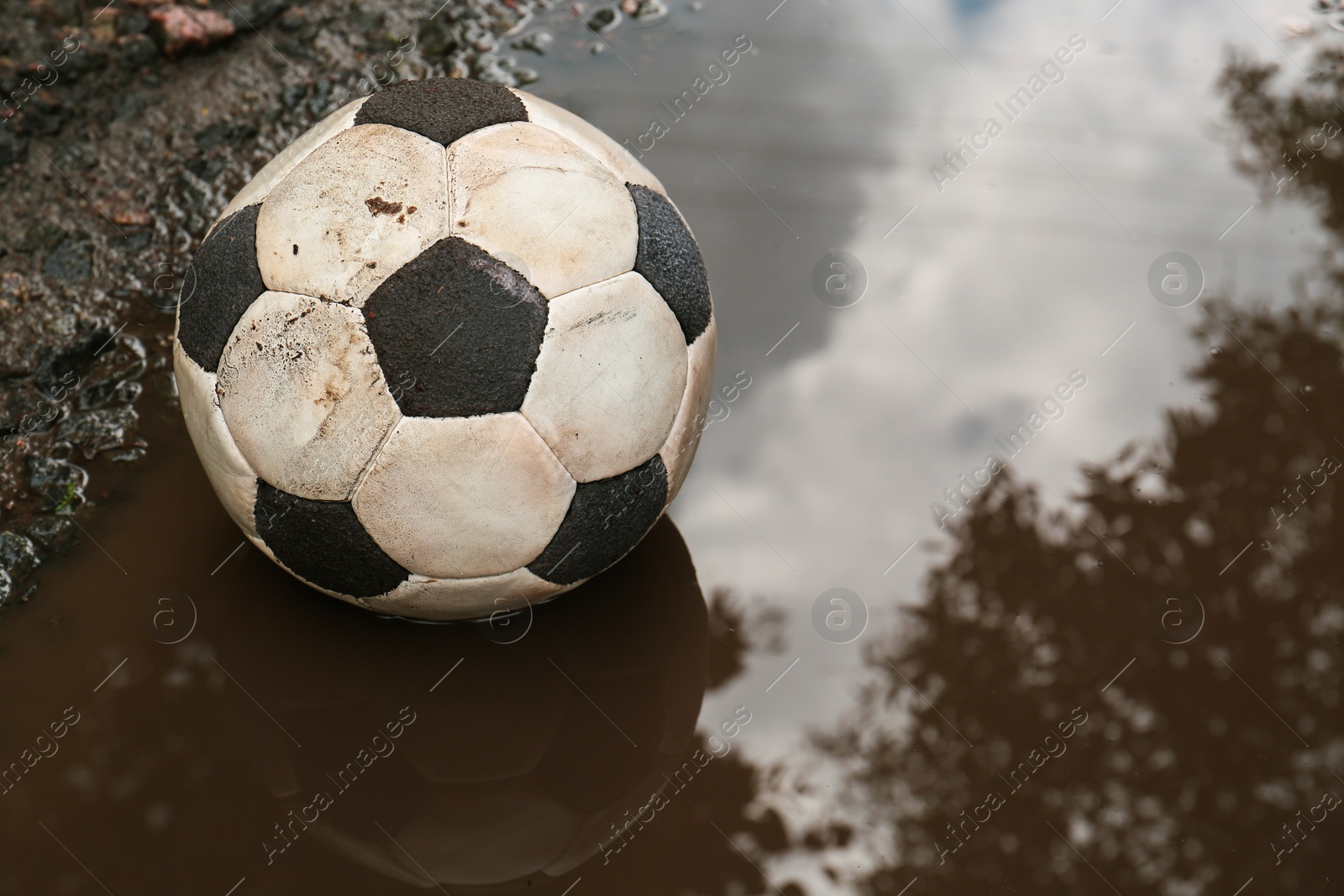 Photo of Dirty soccer ball in muddy puddle, space for text