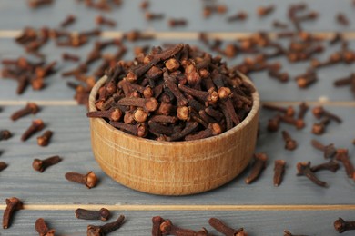 Aromatic dry cloves with bowl on grey wooden table