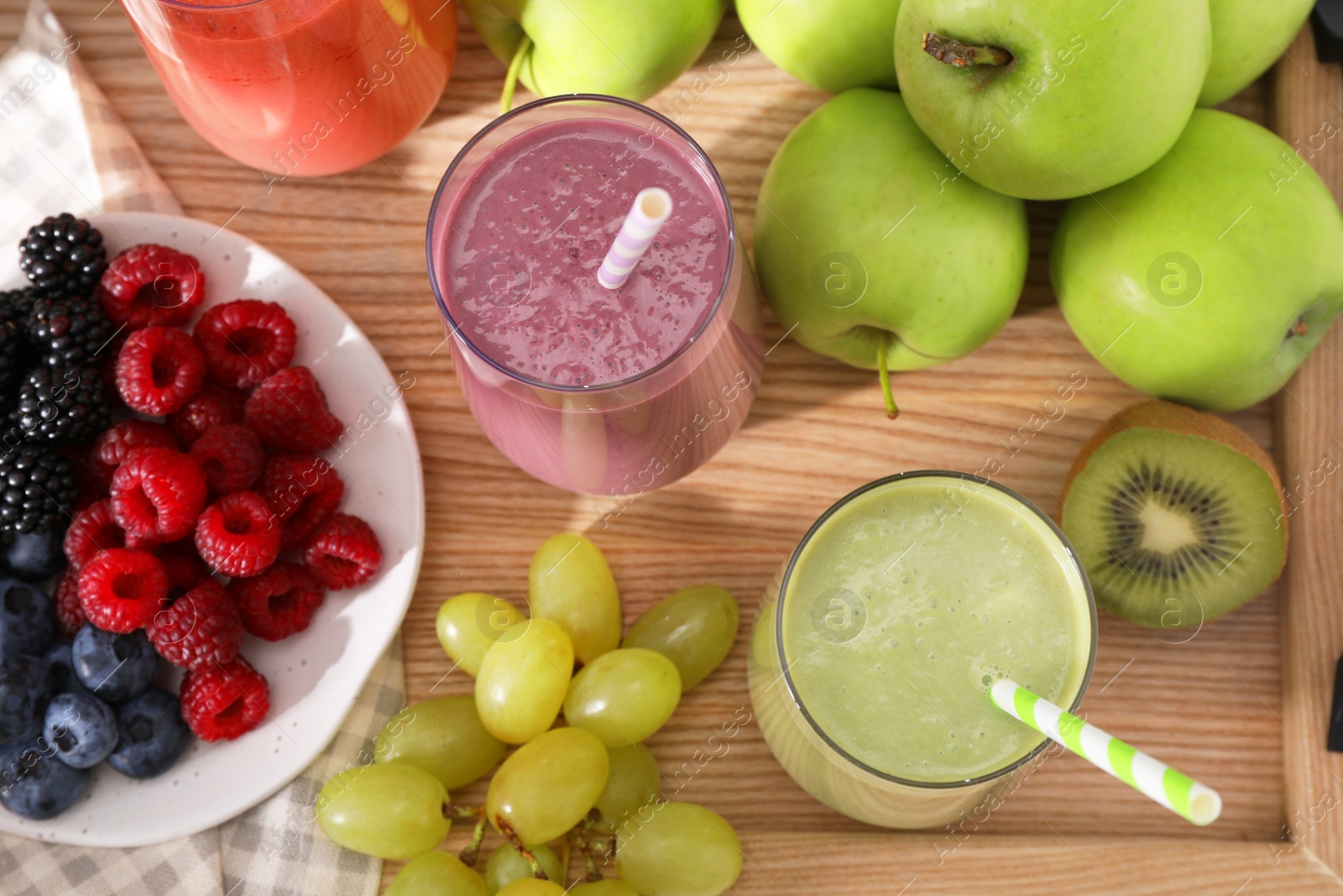 Photo of Glasses of different tasty smoothies and fresh ingredients on wooden table, flat lay