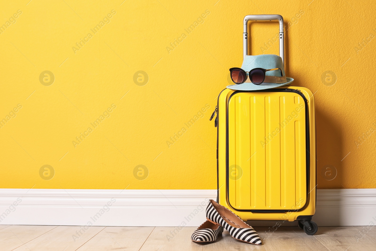 Photo of Bright yellow suitcase with hat, sunglasses and shoes near color wall