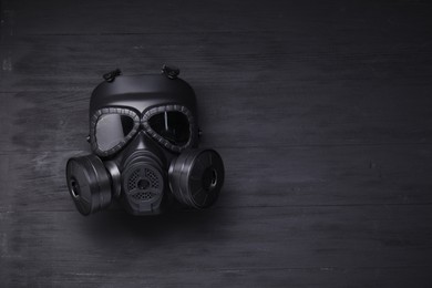 One gas mask on black wooden background, top view. Space for text