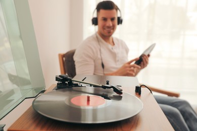Photo of Man listening to music at home, focus on turntable with vinyl record