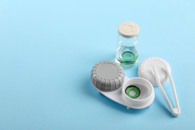 Photo of Bottle of solution, case with green contact lenses and tweezers on light blue background. Space for text