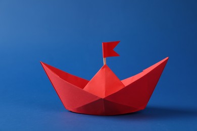 Handmade red paper boat with flag on blue background. Origami art